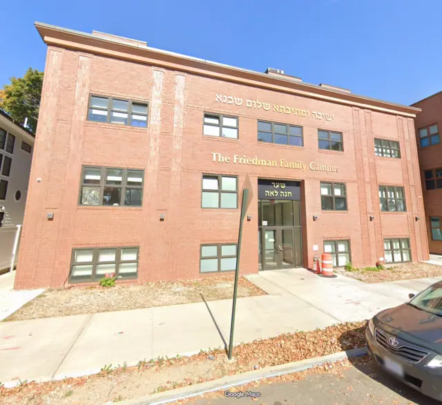 Street View photograph of a brick campus building with a tall central entrance, rows of dark-framed windows and The Friedman Family Campus lettering.