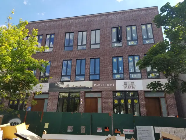 Construction-stage photograph of 346 13th Street showing a red-brick facade, tall windows with installation labels and green site fencing.