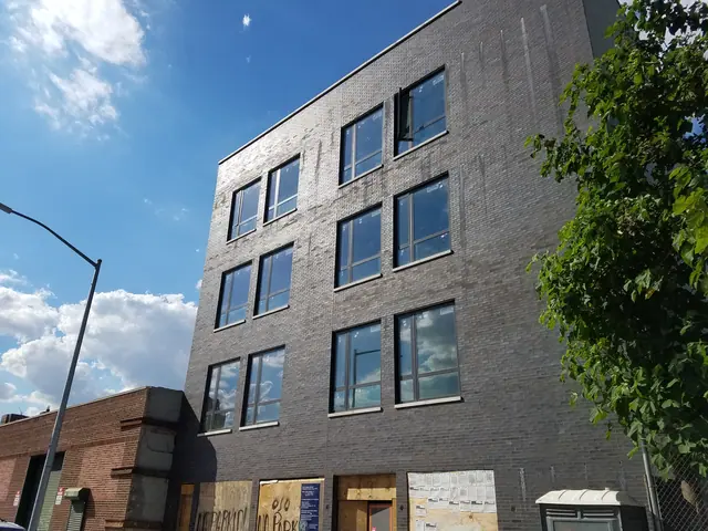Construction-stage photograph of 489 Baltic Street showing a dark-brick facade, large vertical windows, boarded ground-floor openings and a blue sky.