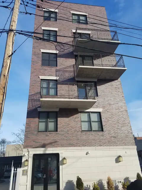 Street view of a red-brown brick building at 543 Brooklyn Avenue, with projecting balconies, black railings, and a pale ground-floor facade.