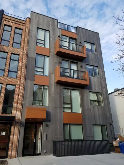 Street view of 657 Quincy Street, showing a gray facade, warm brown balcony surrounds, tall windows, and the entry beside a neighboring brick building.
