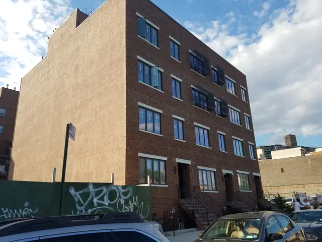 Angled street view of the Gerry Street project, showing its brick facade, broad side wall, black balcony railings, and entry stoops.